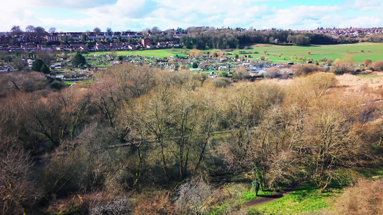 Drone aerial view of woodland and allotments near a town in the UK countryside. Scenic landscape showing trees farmland and residential edge in rural England