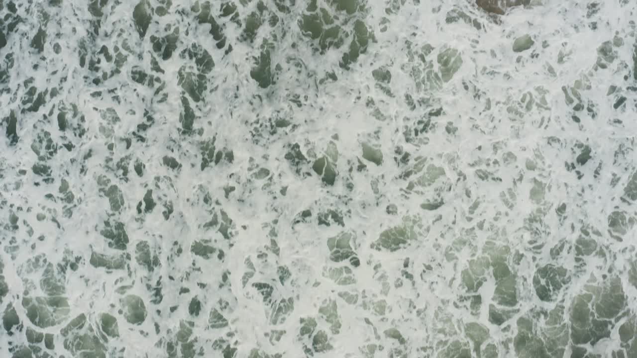 Top-down drone closeup showcases turbulent turquoise waves foaming and swirling across Kuity Beach waters in Odisha's coastal haze
