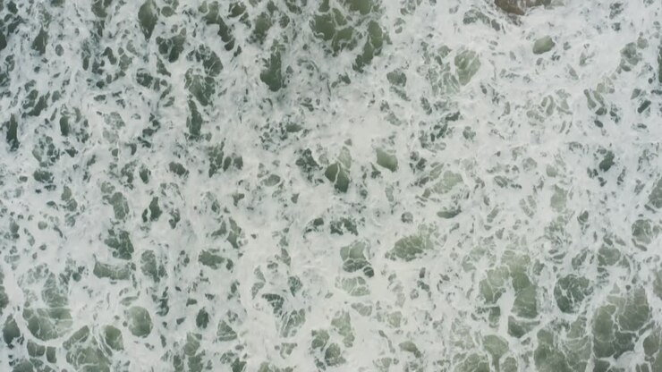 Top-down drone closeup showcases turbulent turquoise waves foaming and swirling across Kuity Beach waters in Odisha's coastal haze