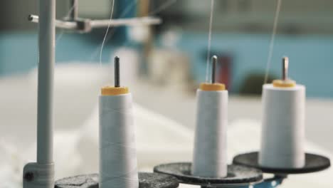 primer plano de hilos blancos en una máquina de coser de fábrica en el fondo de textiles cosidos hechos de tela blanca