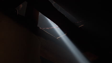 ray of sunlight through crack in roof of shed with wires and rafters. dusty, darkness with sunbeam coming through opening in ceiling. light piercing darkness.