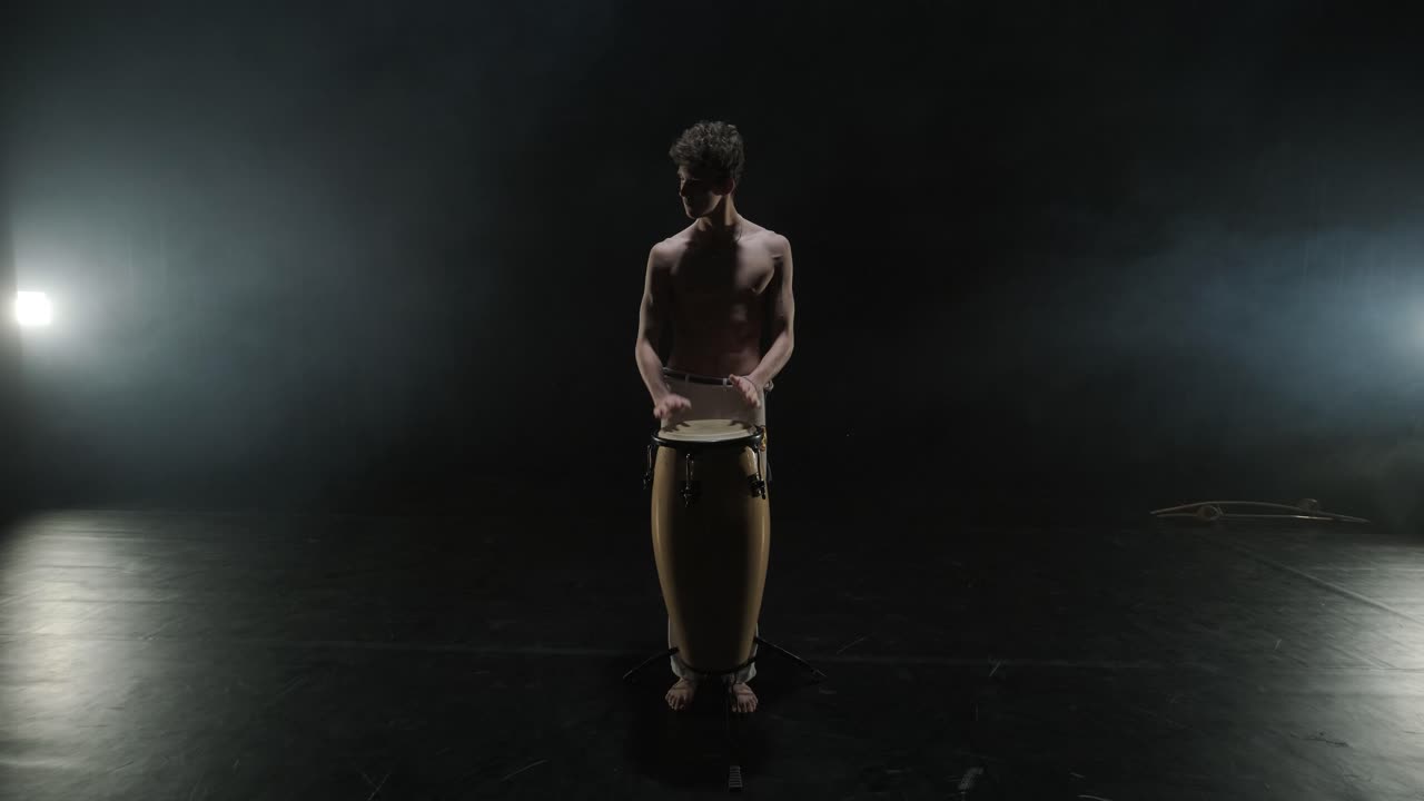 Group of a professional dancers are practicing capoeira in darkness against a spotlight on a black background of studio. Afro-Brazilian martial art that combine elements of dance.