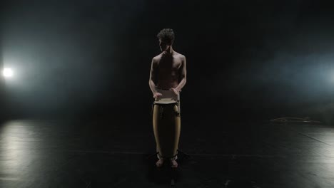 group of a professional dancers are practicing capoeira in darkness against a spotlight on a black background of studio. afro-brazilian martial art that combine elements of dance.