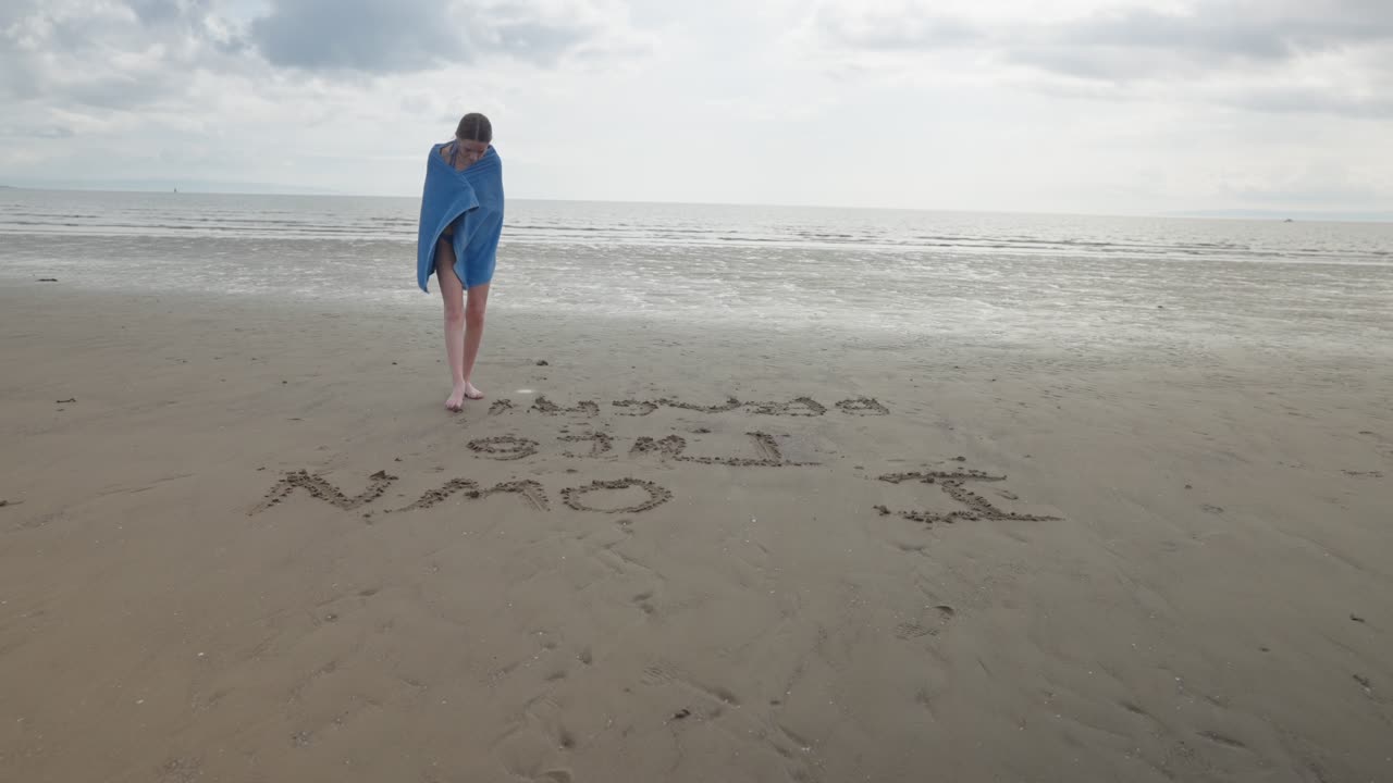 벌거벗은 젊은 여성이 모래 표면에서 단어를 철자, 느린 동작
