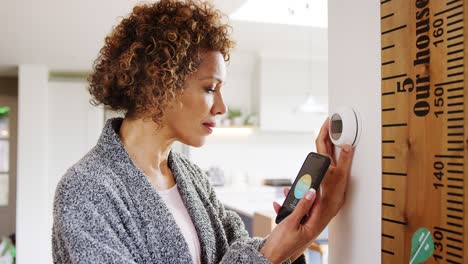 mature woman using app on phone to control digital central heating thermostat at home with gay partner in background - shot in slow motion