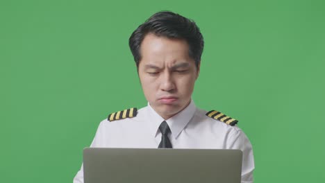 녹색 스크린 배경 스튜디오에 서있는 동안 노트북을 사용하는 아시아 남자 조종사의 가까운 사진