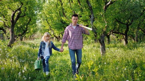 Un-Agricultor-Con-Una-Hermana-Menor-Camina-Por-El-Huerto-De-Manzanas-Con-Una-Guadaña-Y-Una-Regadera