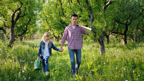 un granjero con una hermana menor camina por el huerto de manzanas con una guadaña y una lata de agua