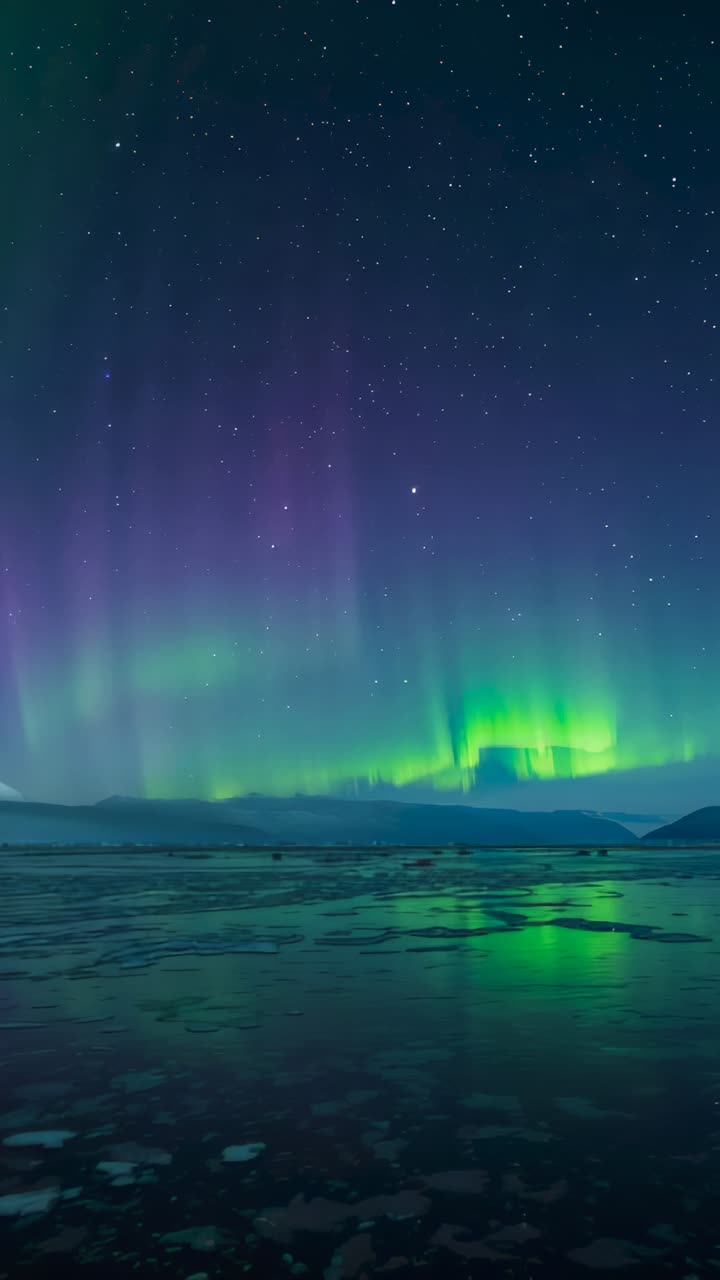 Vertical video: Arriving solar wind energizing aurora borealis over polar lake, mirroring on ice