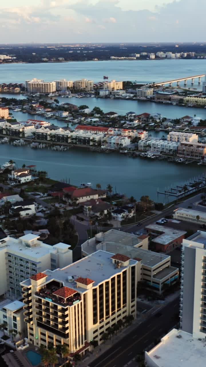 Tall hotels and waterfront buildings dominate the cityscape beside a calm blue bay, with bridges and nearby residential areas stretching into the distance
