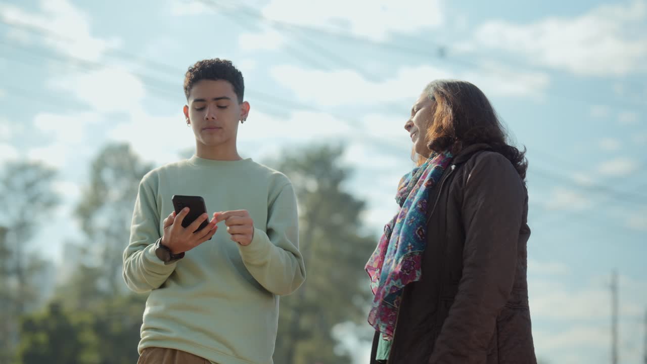 Two people interacting and looking at a smartphone outdoors
