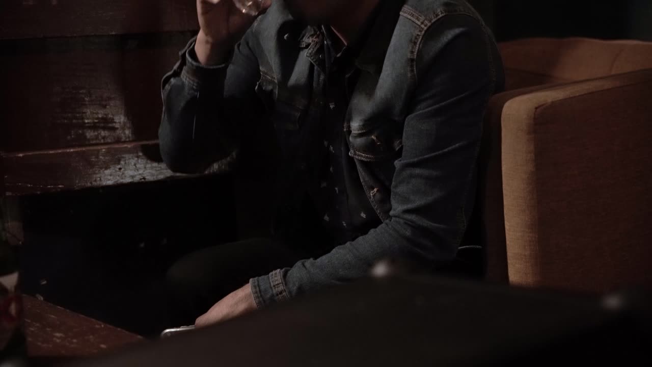 어두운 방에 있는 소파에서 술을 마시는 남자