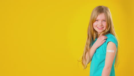 foto de estudio de una niña joven con yeso en el brazo contra un fondo amarillo
