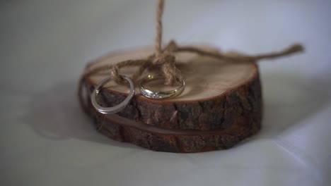 two gold and diamond wedding bands rings on round piece of live edge wood and tied together with brown twine before wedding ceremony