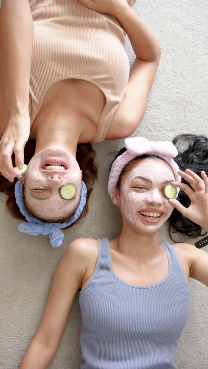 Vertical video: Relaxing at home, two girls enjoying face masks with cucumber slices