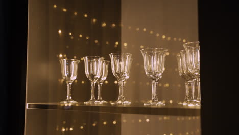 Close-Up-View-Of-Several-Empty-Crystal-Glasses-On-Wooden-Table,-Reflected-Christmas-Lights-1