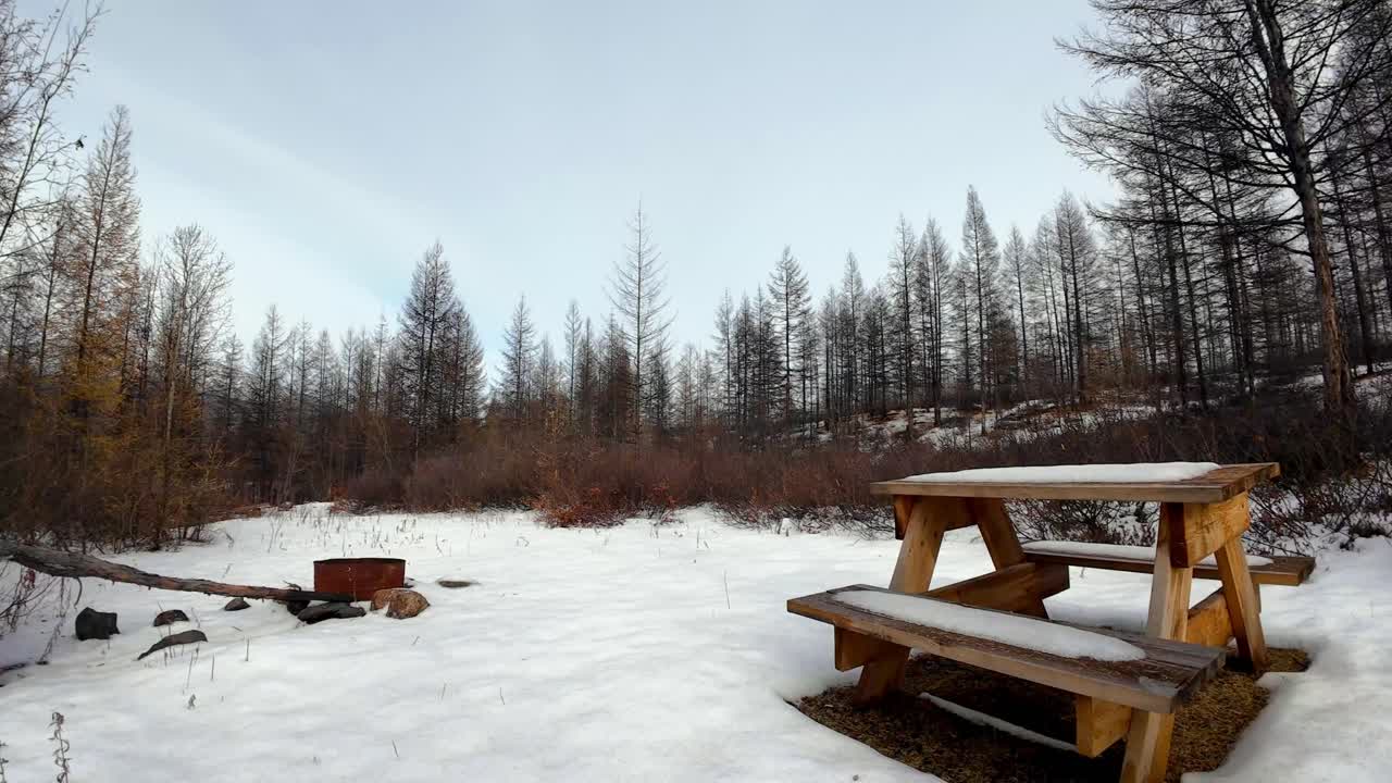 Ett snötäckt picknickbord står stilla och rofyllt i ett vinterlandskap. Scenen framkallar en tyst, lugn atmosfär