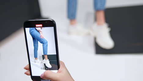 taking mobile phone video of a girl demonstrating modern sport shoes. stylish casual look in the studio.