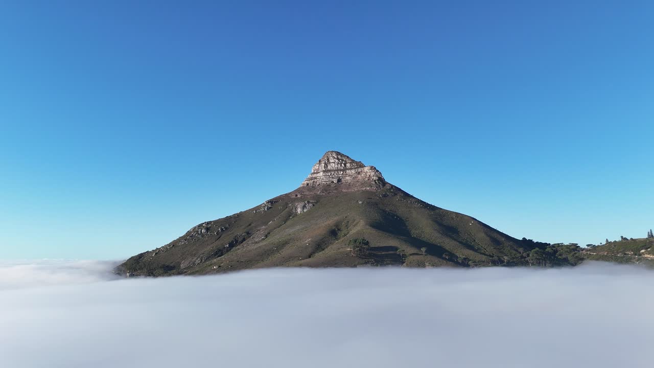 Aerial of Lion’s Head mountain in Cape Town, South Africa, appearing from the clouds surrounded by mist with only the peak emerging above the fog
