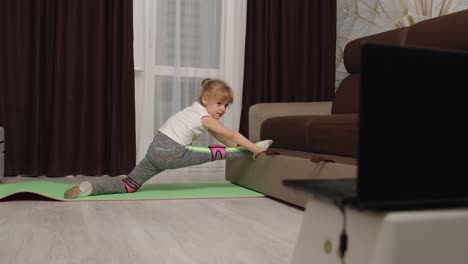 Niña-Haciendo-Ejercicios-Deportivos-Con-Hilo,-Viendo-Lecciones-De-Educación-En-Línea-En-Video-En-Una-Computadora-Portátil-En-Casa