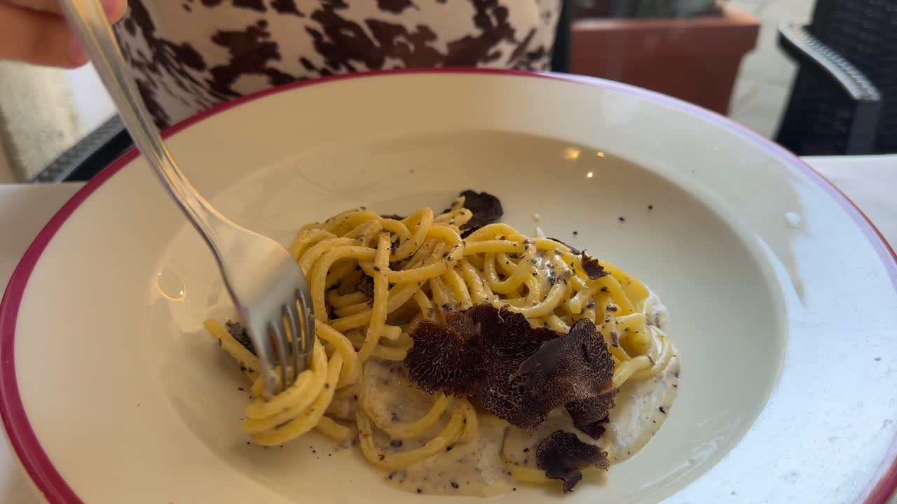 Forchetta che avvolge spaghetti gourmet con scaglie di tartufo nero.