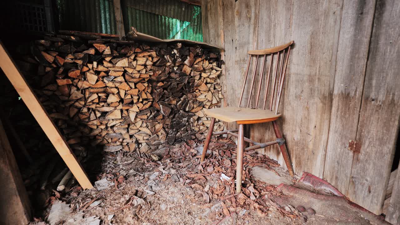Chair stands by wall, chopped firewood in shed rustic stillness, Latvian village