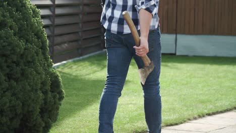 un joven con jeans azules y una camisa azul camina con el hacha en la mano