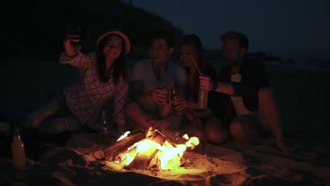 picnic of young people with bonfire on the beach in the evening. cheerful friends taking pictures on the phone. slow motion shot