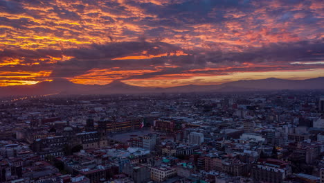 Aerial-hyperlapse-of-colorful-sunrise-in-historical-center-with-the-Zocalo-main-square-the-Mexican-flag-and-the-volcanoes-at-the-back