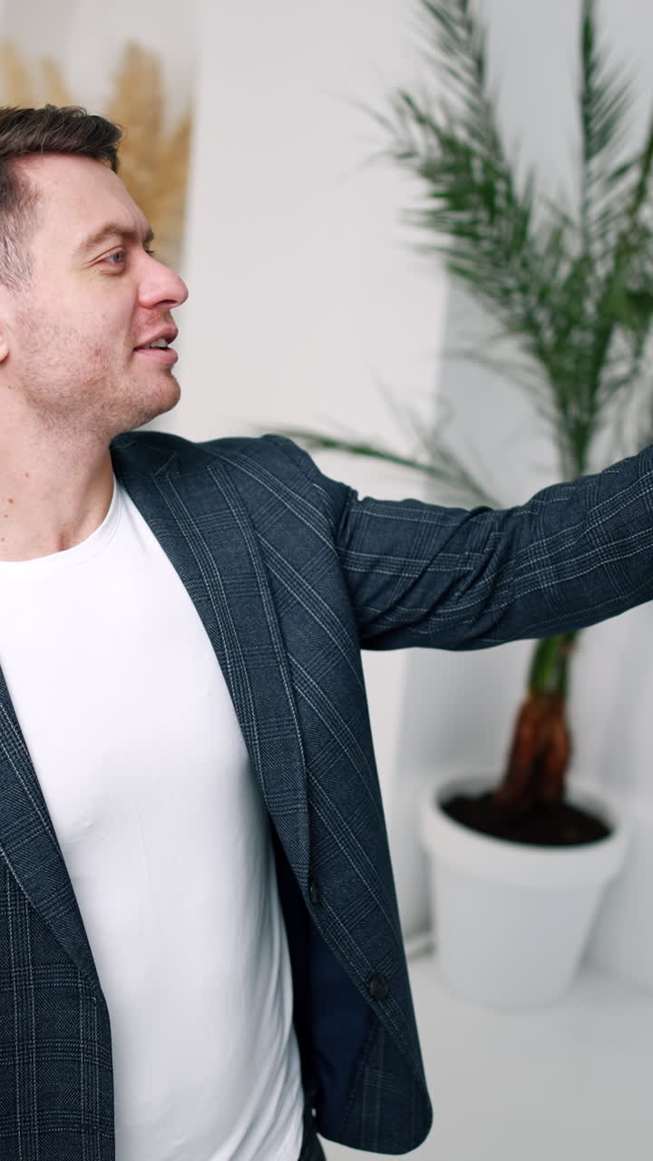 Athletic Caucasian man having video conversation. Man points at something behind him and turns to the sides. Vertical video