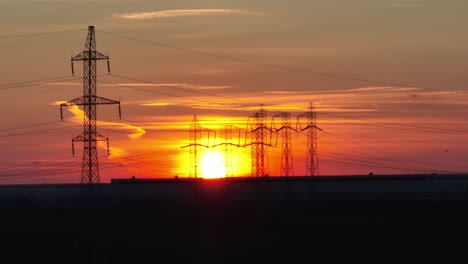 tiro ascendente de drones de torres de transmisión en el campo frente al sol de color naranja
