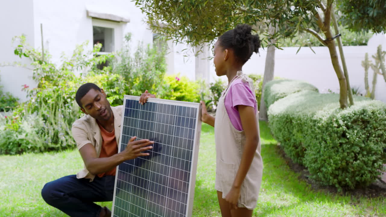 African american father and daughter installing solar panel in garden, enjoying sunny day in garden
