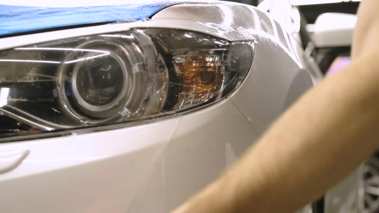 hombre cubriendo el coche con cinta de poliuretano de vinilo. películas para el coche. pegatina película protectora en el faro del coche