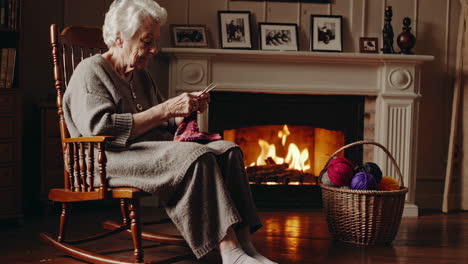 senior woman knitting by the fireplace