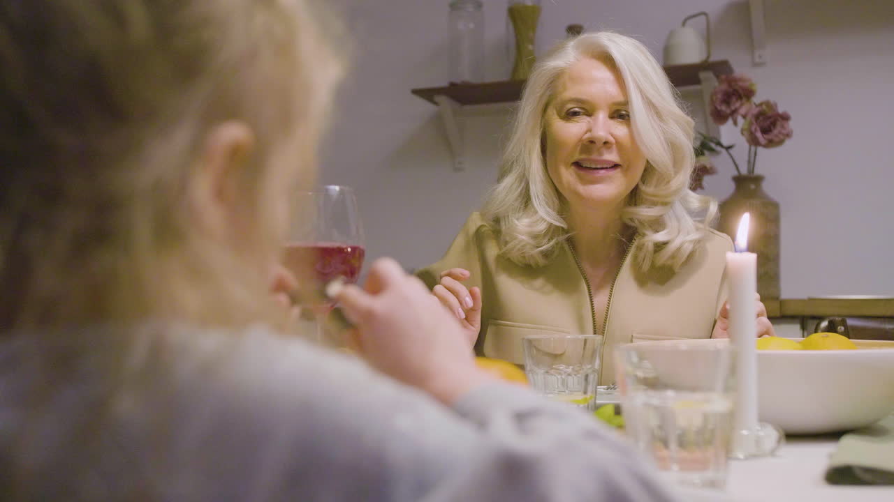 Rear View Of A Kid Sitting At Table During A Family Dinner And Talking With A Mature Woman 1