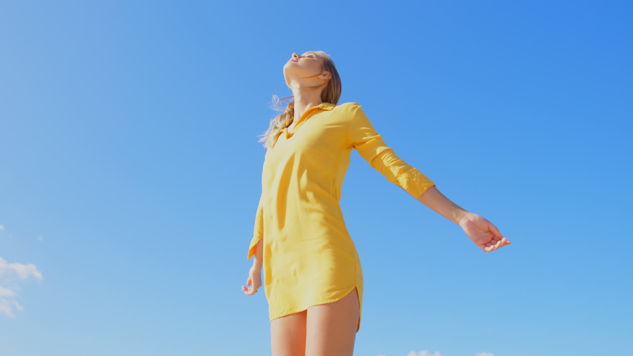 해변 4k에 팔을  ⁇ 고 서있는 젊은 백인 여성의 낮은 각도 뷰