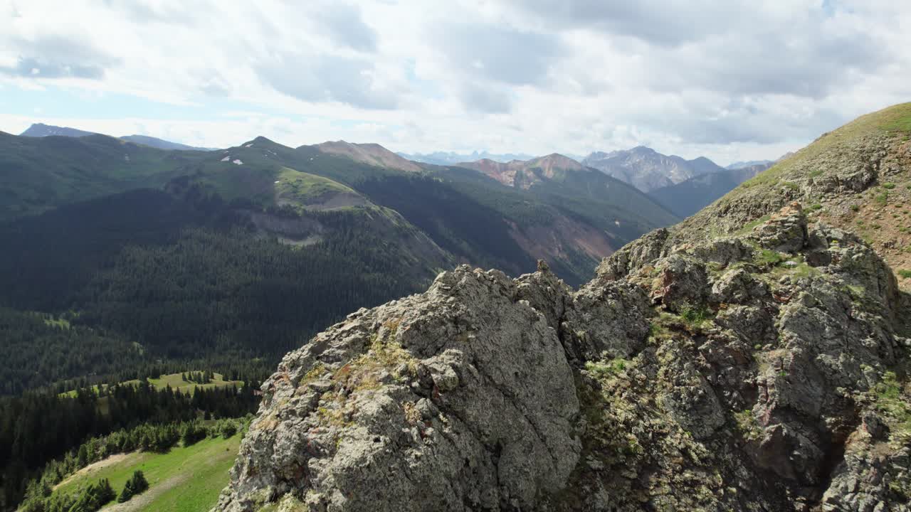 A slow rising and rotating drone flyover of a rock outcropping, revealing the Million Dollar Highway (Red Mountain Pass) in the valley below, in the San Juan Mountain Range, Colorado