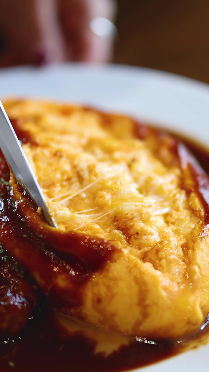 Primo piano di omurice affettato, che rivela l'interno morbido dell'uovo, in un'atmosfera calda di ristorante.