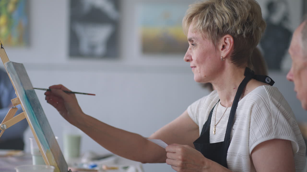 An old retired woman paints a picture together with friends. An elderly group of friends and a senior woman are drawing pictures together.