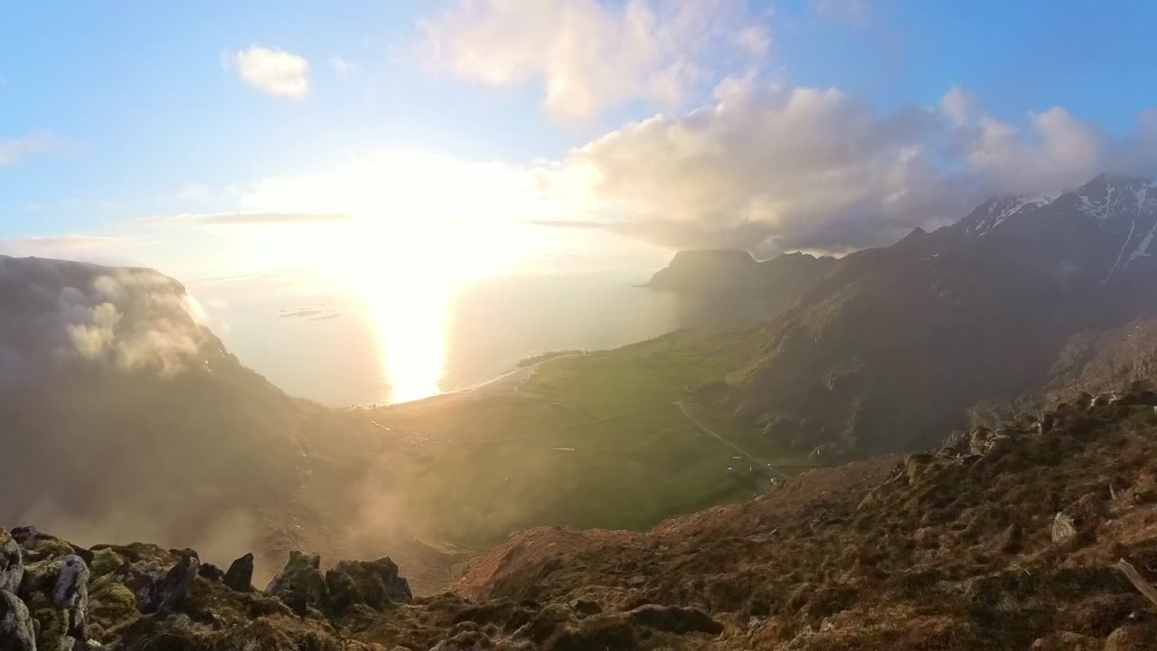 Ocean fog moves from sea across Utakleiv village and beach, climbing uphill toward camera. Midnight sun