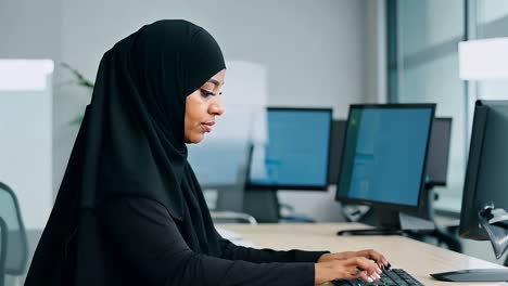 a woman in a hijab working at a computer in an office