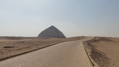 sandy yellow desert with ancient egyptian bent pyramid on the horizon, egypt