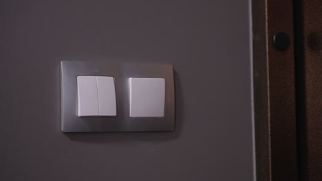 close-up of woman hand pressing light switch in dimly lit room, soft ambient glow highlights fingers as she turns on the light, creating a contrast between darkness and illumination