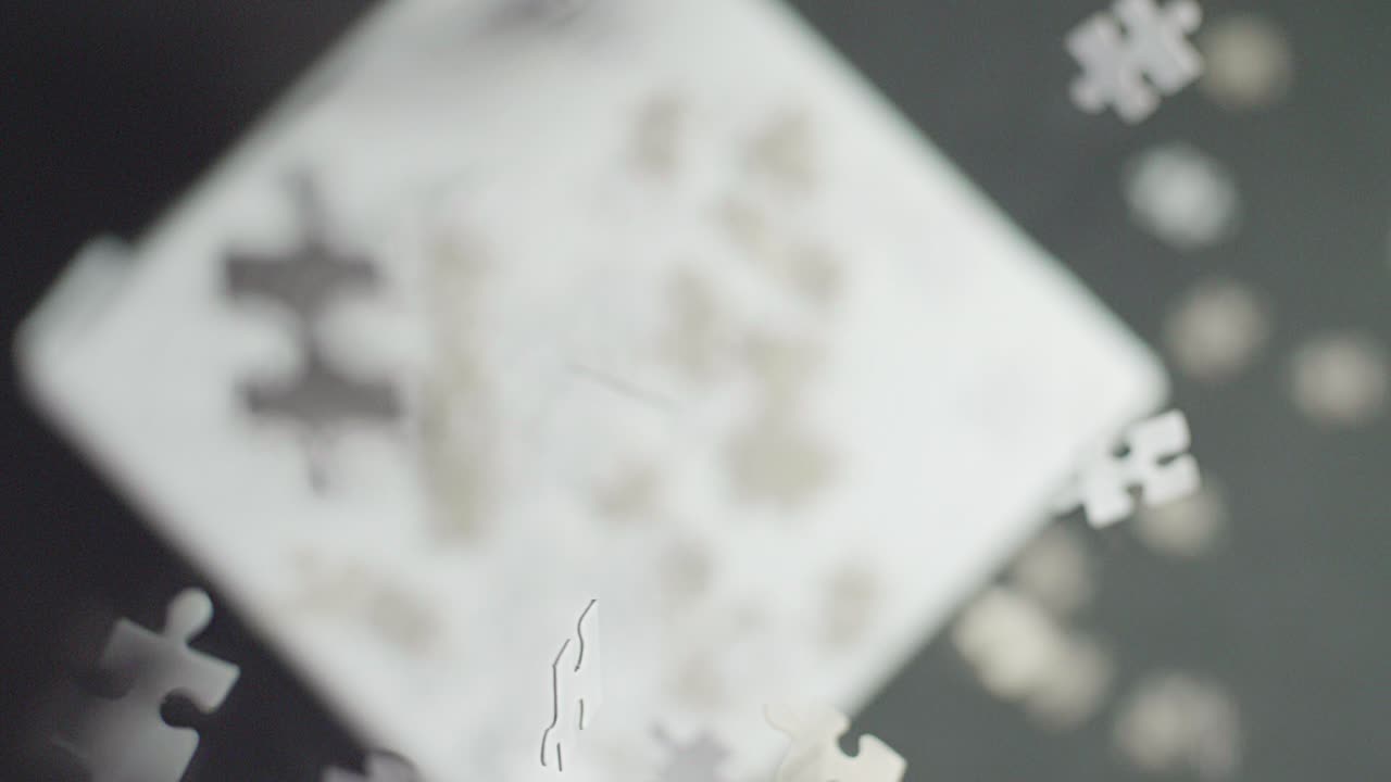 흰색 및 회색 퍼즐 조각이 흰색 표면에 떨어지고 초점이 맞지 않고 어두운 배경으로 튀고 회전합니다.