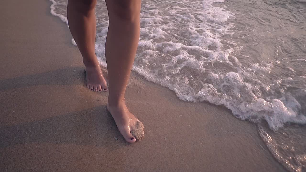 chica descalza camina sobre la arena y las olas ruedan en cámara lenta