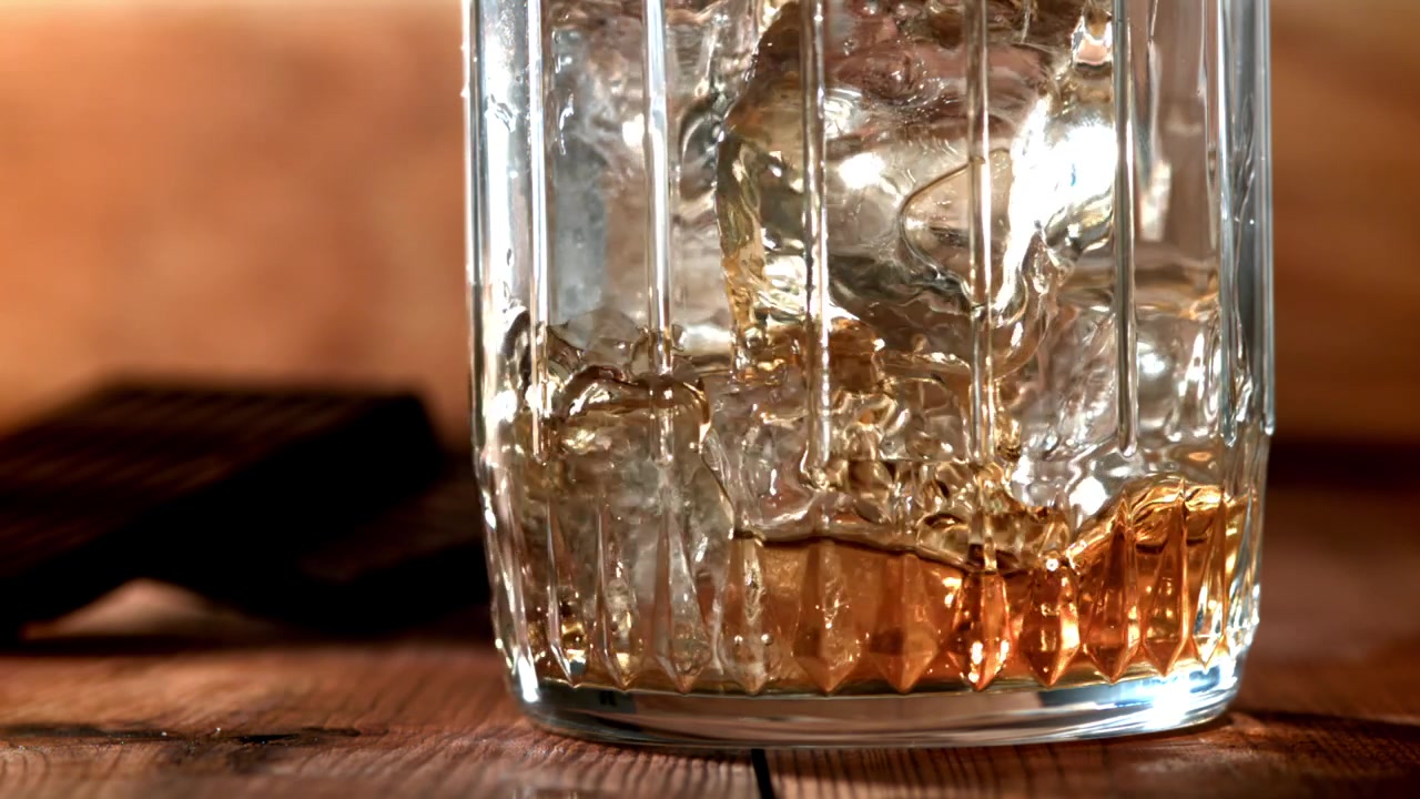 Versamento al rallentatore di whisky dorato in un bicchiere con ghiaccio.