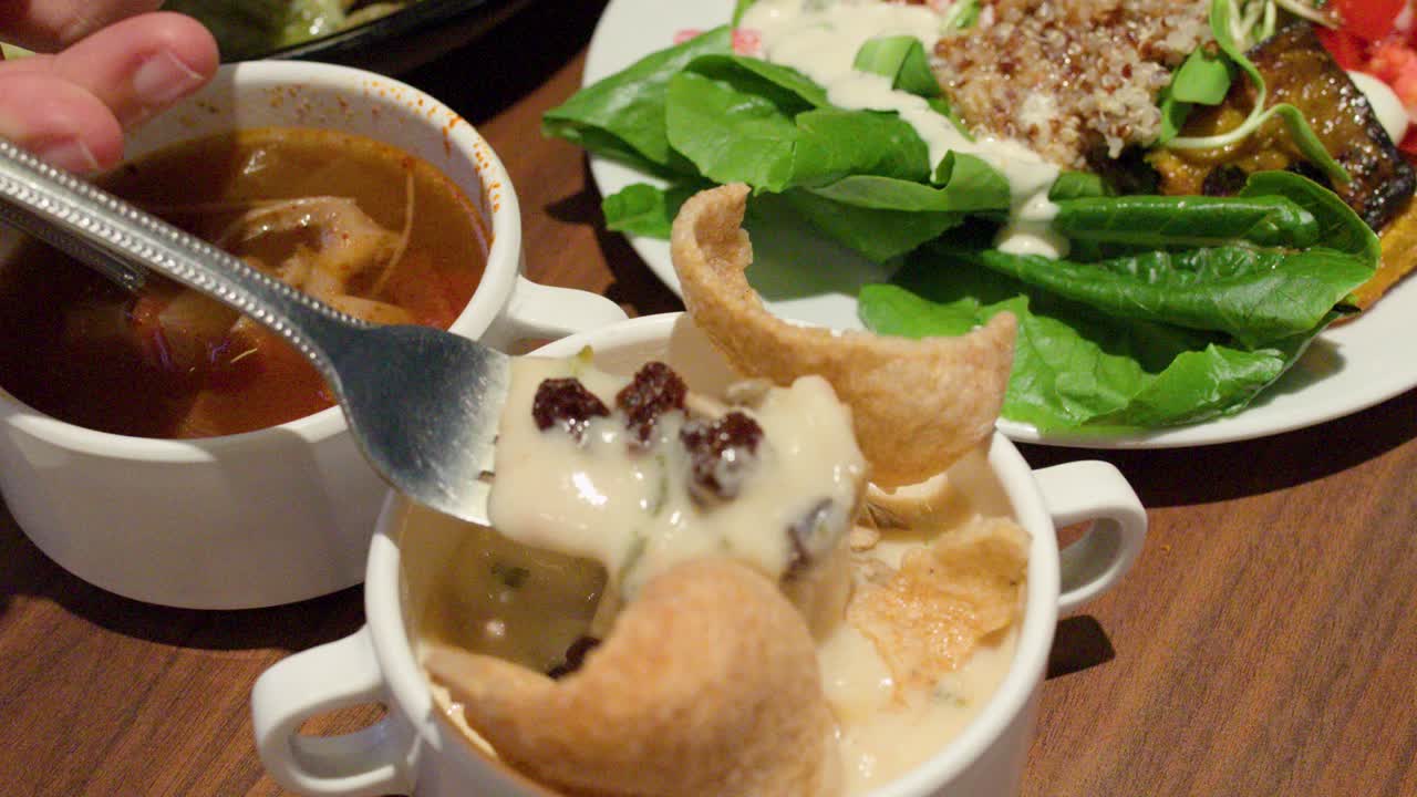 Hand lifts stretchy creamy pasta from soup bowl at casual buffet restaurant table setting