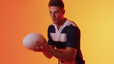 caucasian male rugby player catching rugby ball over orange lighting