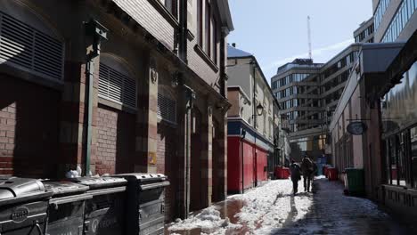 Two-people-walking-in-sunny-back-street-as-snow-melts,-Sheffield,-wide-angle