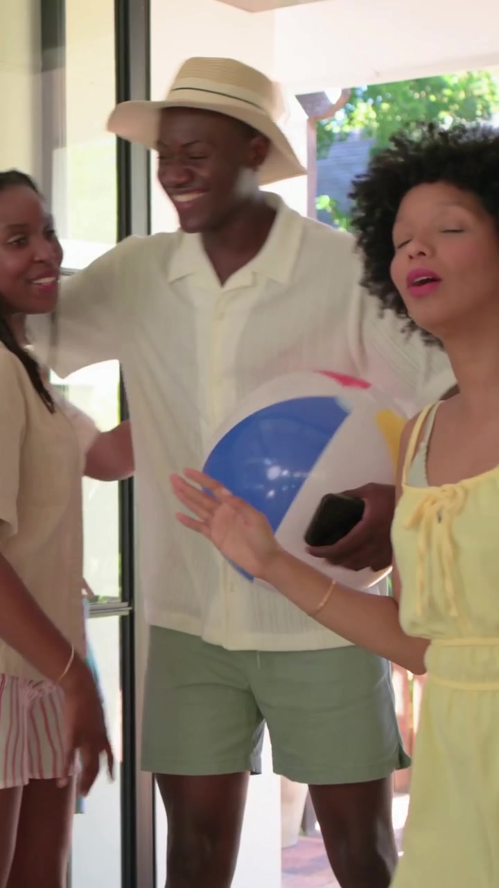 Vertical video: Friends entering via glass door passing ball waving with emoji faces for home visit